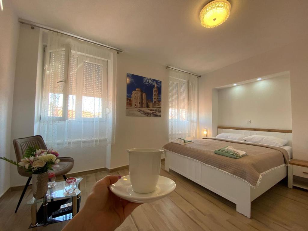 una persona che tiene una tazza in una camera con un letto di Jeta Studio & Rooms a Zara (Zadar)