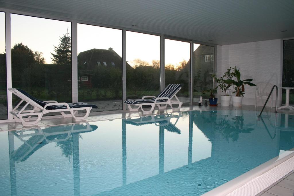 a swimming pool with two lawn chairs and windows at Ferienwohnungen im Hotel garni zur Post in Utersum