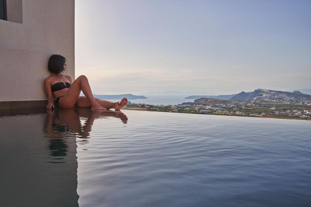 a woman sitting on the edge of a swimming pool at Apikia Santorini in Pirgos