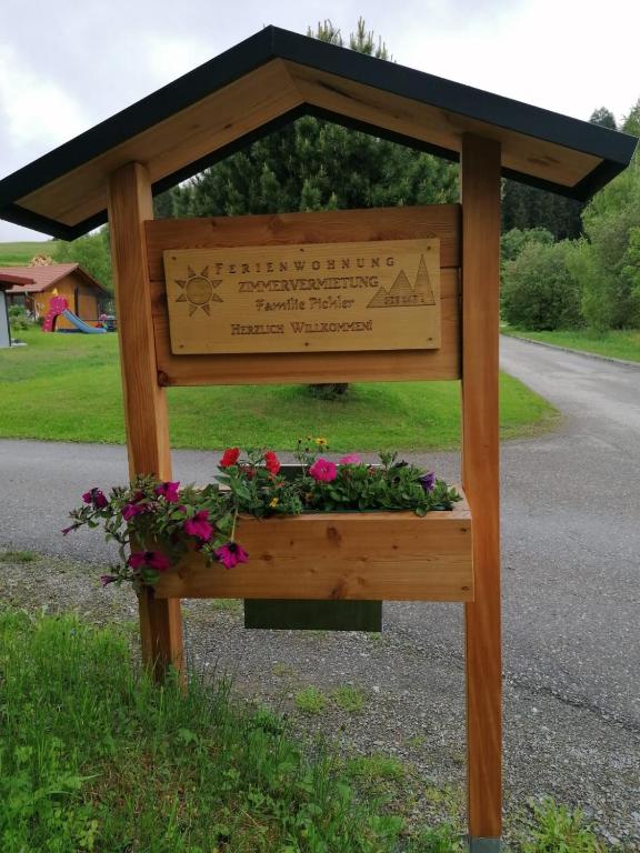 a wooden structure with a sign and flowers on a road at Ferienwohnung Familie Pichler in Neumarkt in Steiermark