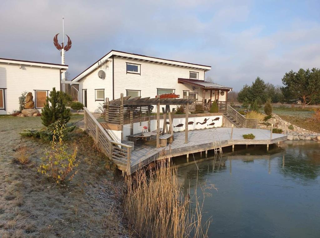 ein Haus mit einer Holzbrücke über einen Wasserkörper in der Unterkunft Villa Feniksas in Poškai