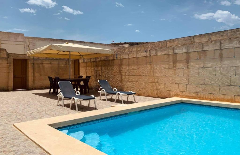 a swimming pool with chairs and a table and an umbrella at Andar Farmhouse in Victoria