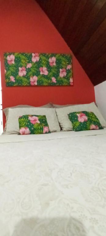 a bed with two pillows and a red wall at Chalé Rancho Aratama in Jacareí