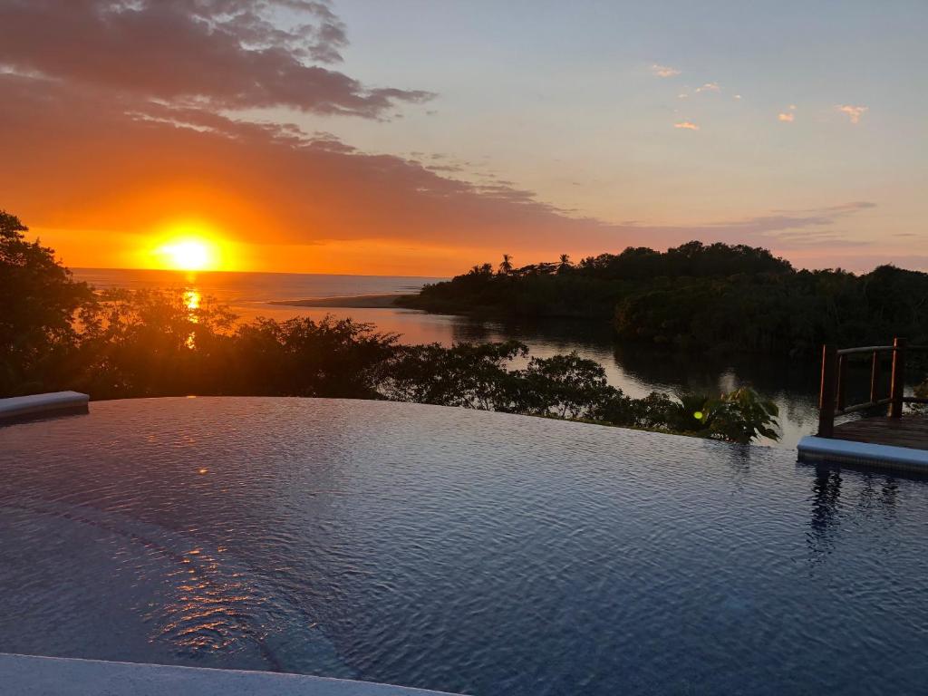 a pool with a sunset in the background at Casa Caletas Boutique Hotel in Puerto Coyote
