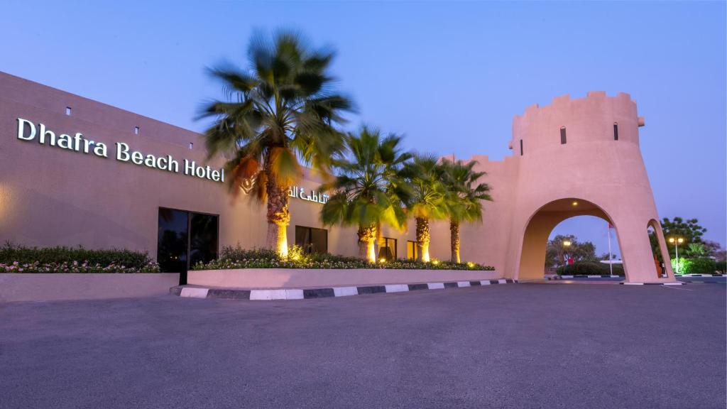 a beach house with palm trees in front of it at Dhafra Beach Hotel in Jebel Dhanna