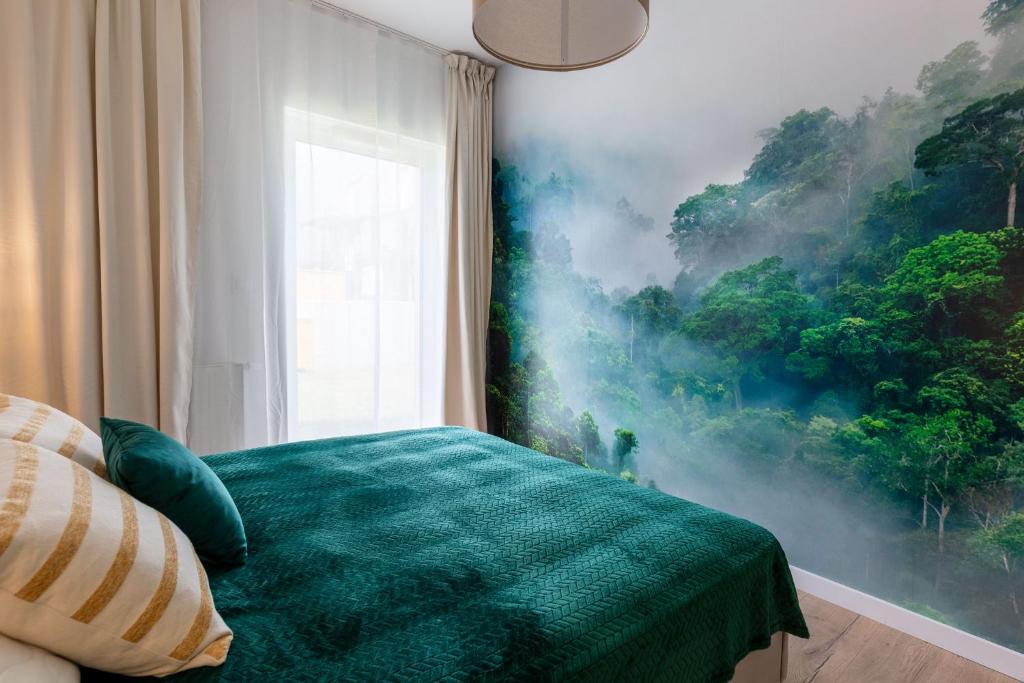 Corner bedroom view showing window with sheer curtains, green quilted bedspread and misty forest wall mural.