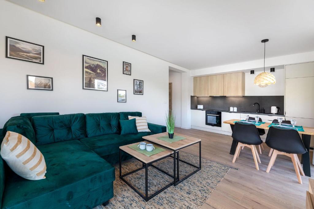 Open-plan living area with emerald sectional sofa, nested coffee tables, dining table and modern kitchen.