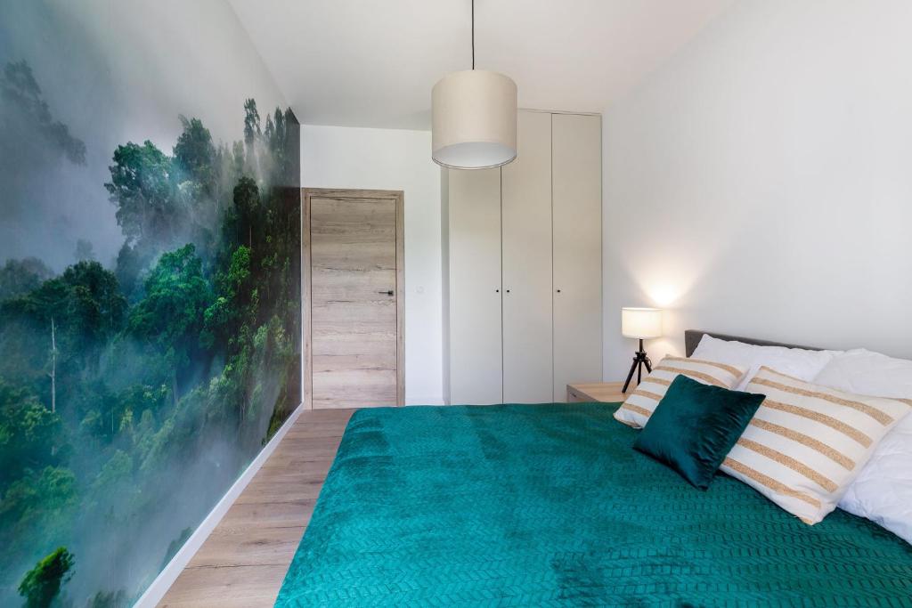 Bedroom with emerald green bedspread, striped pillows, bedside lamp and large forest mural covering one wall.