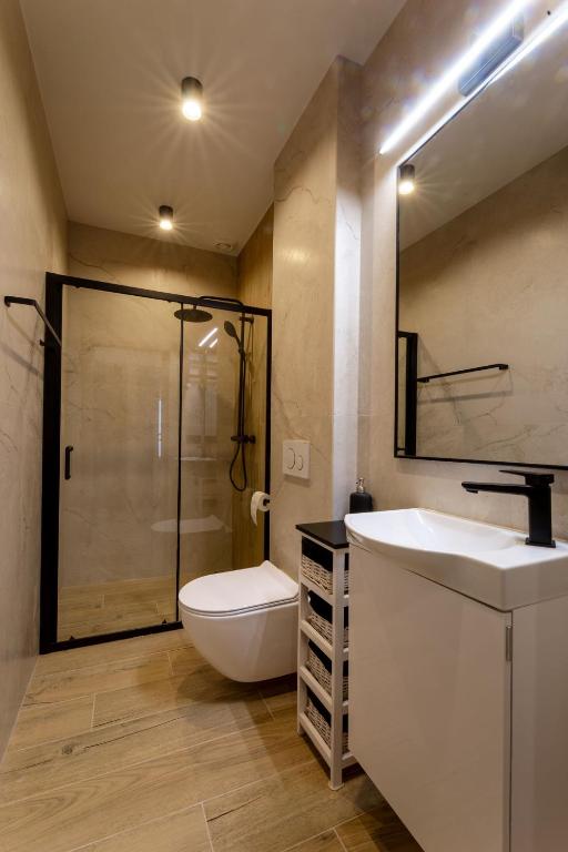 Compact narrow bathroom with glass-framed shower, wall-mounted toilet, small vanity and wicker storage unit.