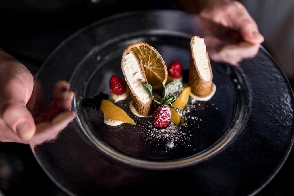 a person holding a plate of food with fruit on it at Hotel Genziana in Selva di Val Gardena