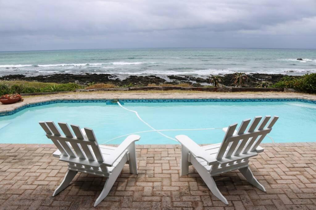 2 sillas sentadas junto a una piscina con el océano en Oceans End - a home on the beach, en Kini Bay