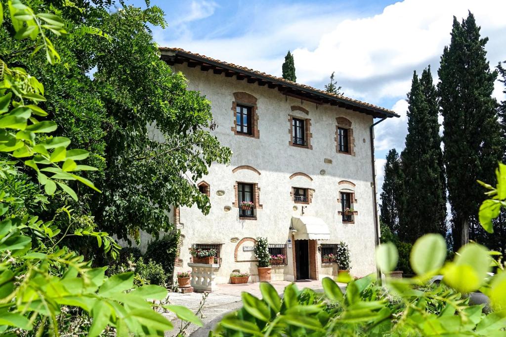 un gran edificio blanco con árboles delante de él en Torciano Hotel Vecchio Asilo, en San Gimignano