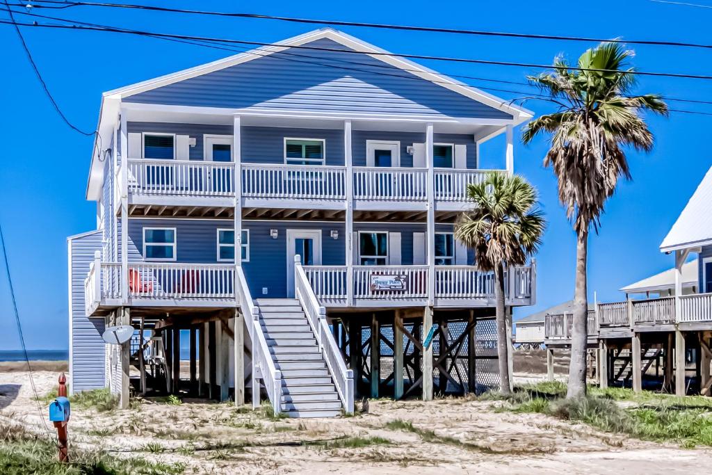 uma casa azul na praia com palmeiras em Malibu Beach House em Dauphin Island