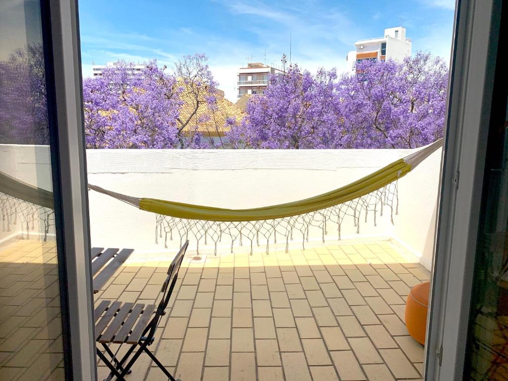 a hammock on a balcony with purple trees at The Central Guesthouse in Faro
