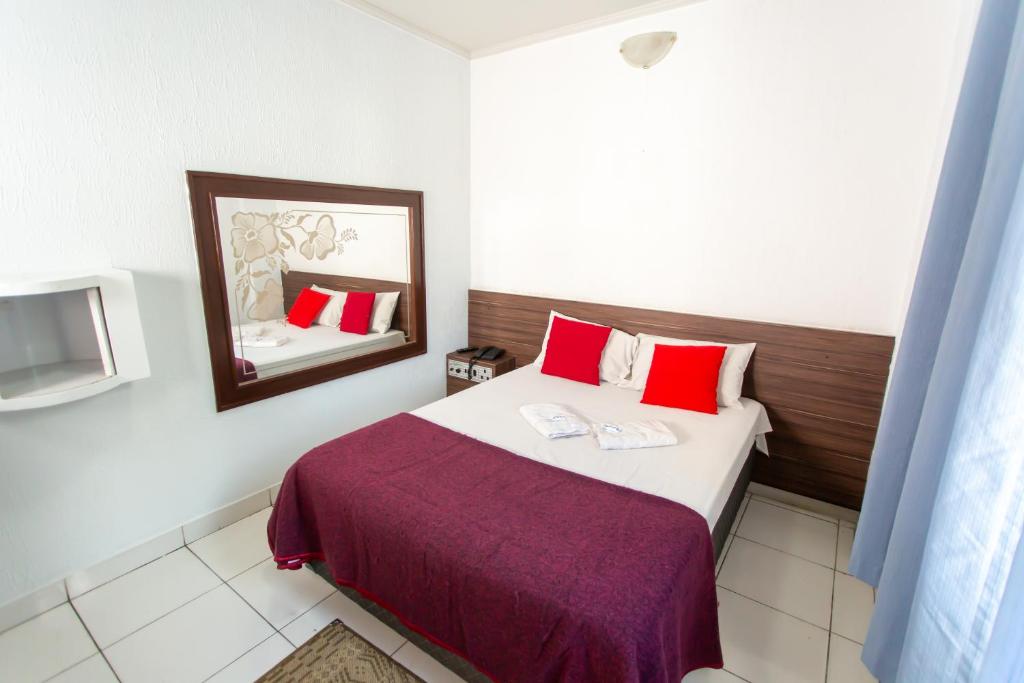 Schlafzimmer mit einem Bett mit roten Kissen und einem Spiegel in der Unterkunft Hotel Cambará - By UP Hotel in Osasco