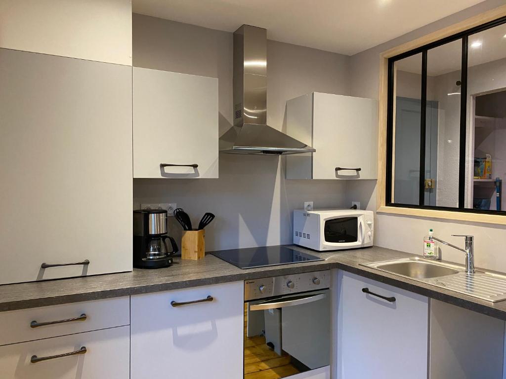 een keuken met witte kasten, een wastafel en een magnetron bij Appartement équipé au centre de Bletterans in Bletterans