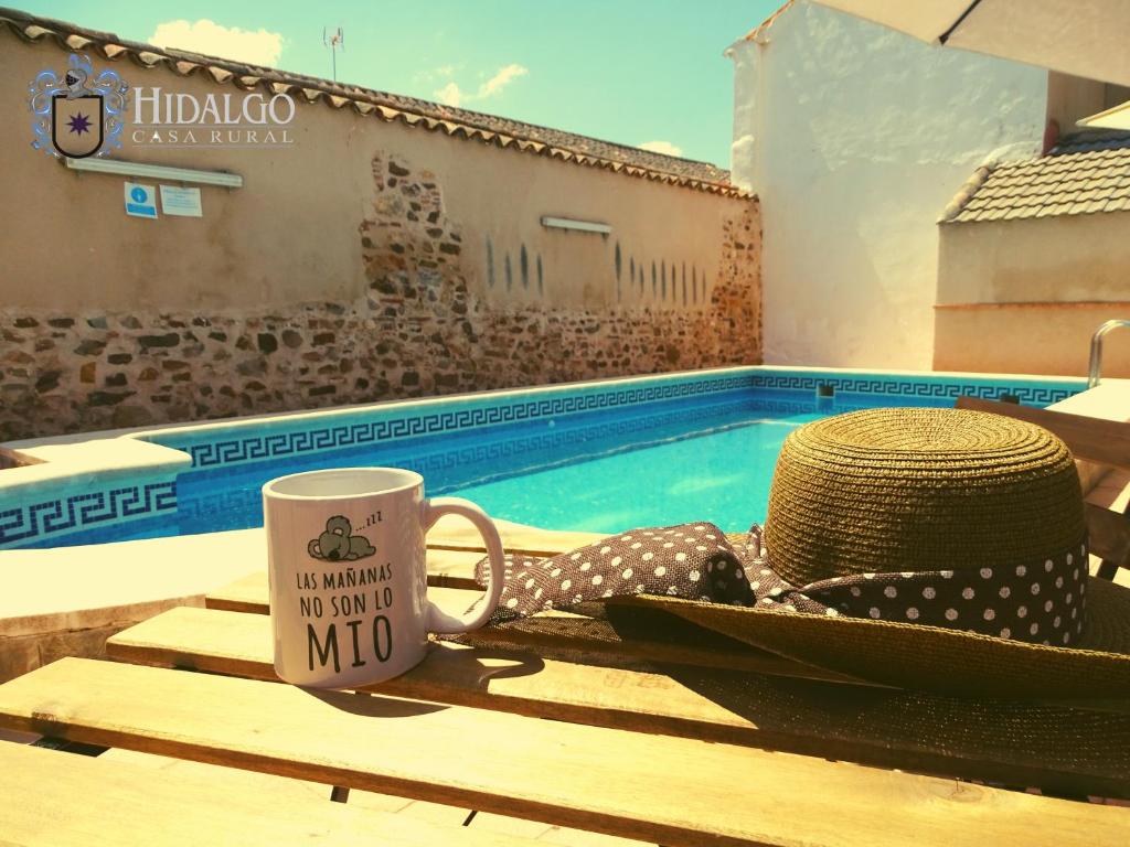 una taza de café y un sombrero sentado en una mesa junto a una piscina en Casa Rural Hidalgo, en Ciudad Real