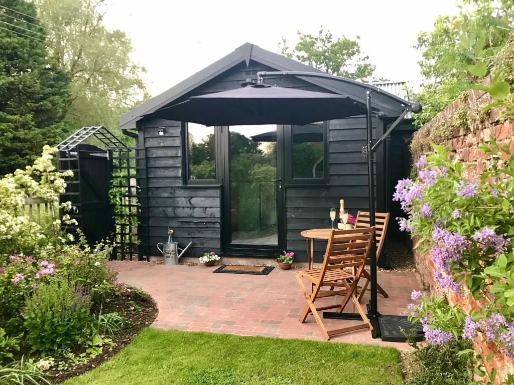 a black shed with a table and an umbrella at Melford Allotment Shed-Vintage Lodge Suffolk in Long Melford