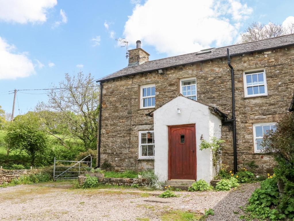 an old stone house with a red door at Spout Cottage in Sedbergh