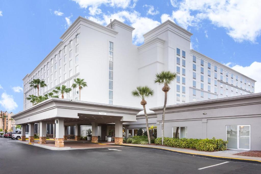 Holiday Inn & Suites Across From Universal Orlando, an IHG Hotel في أورلاندو: مبنى ابيض كبير امامه نخيل