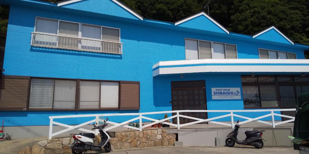 Guest House Shiraishi في Kasaoka: مبنى ازرق به اثنين من الدراجات البخارية متوقفة أمامه