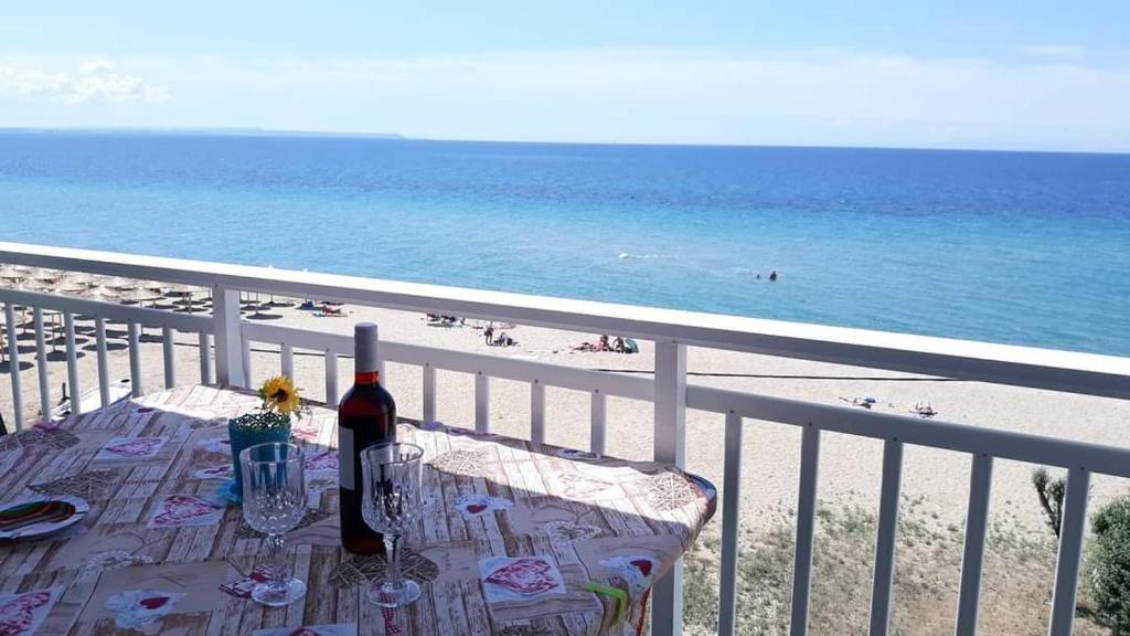 Vasileiadou Coastal Rooms في فلوغيتا: طاولة مع زجاجة من النبيذ على شرفة مع الشاطئ