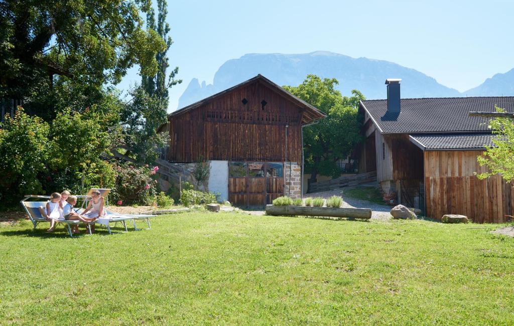 two people sitting on chairs in a yard with a barn at Huberhof in Völs am Schlern