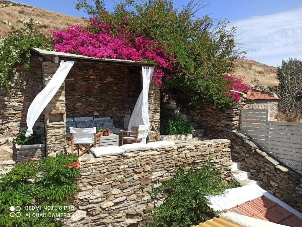 a stone wall with a patio with chairs and flowers at Hidesign Athens Traditional Stone House in Kea's Port in Korissia