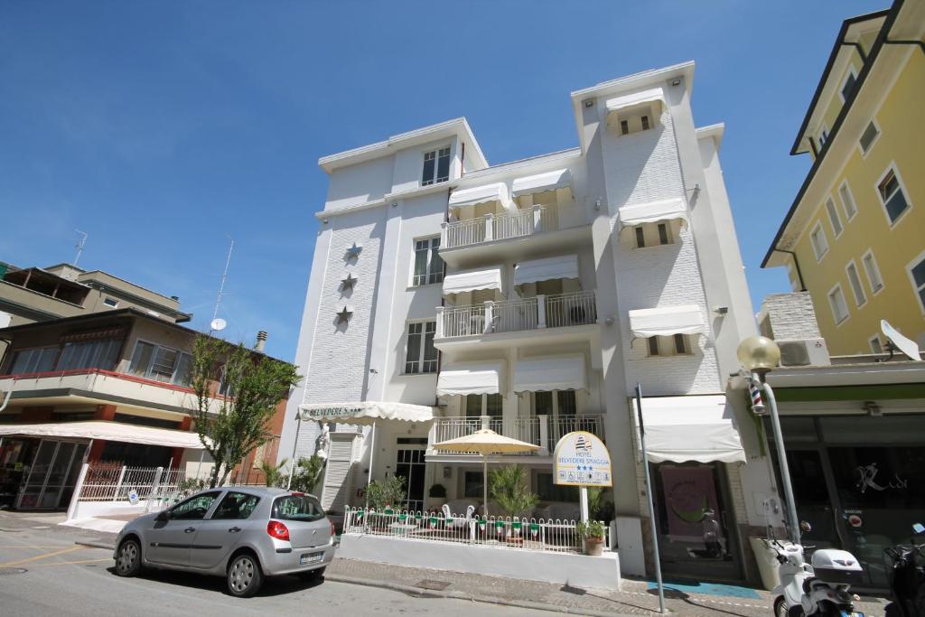 a white building with a car parked in front of it at Hotel Belvedere Spiaggia in Rimini
