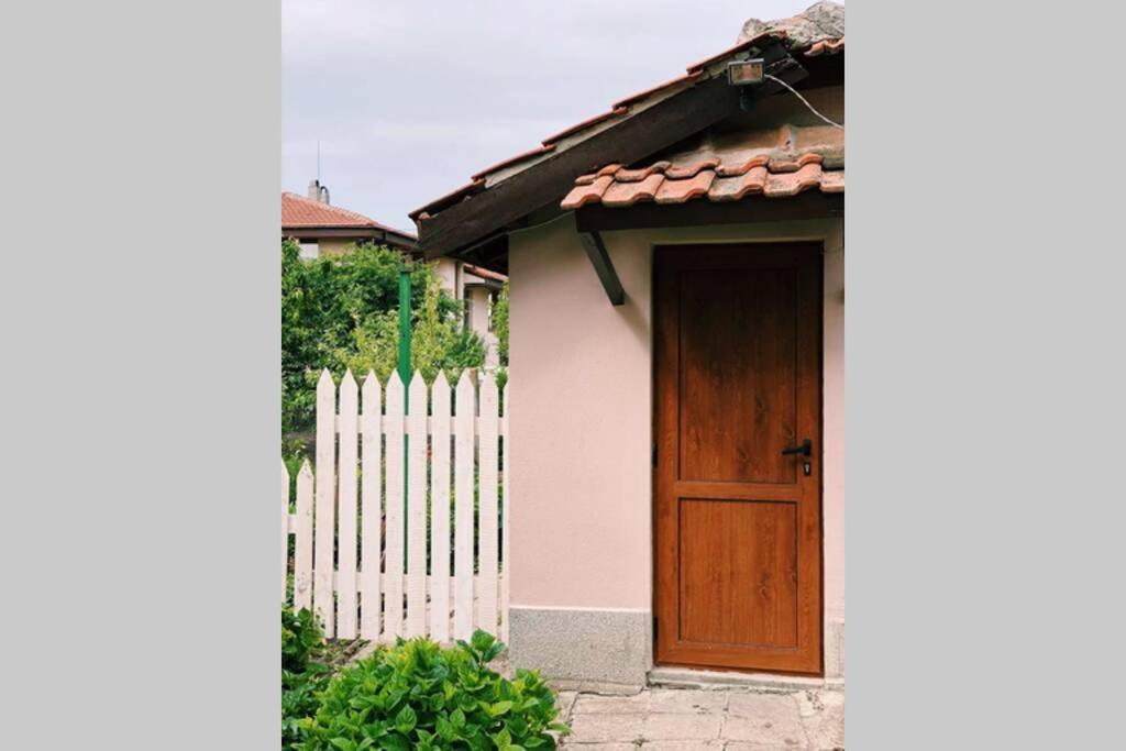 una casa con una puerta de madera junto a una valla blanca en Cute Little House with a White Picket Fence, en Burgas