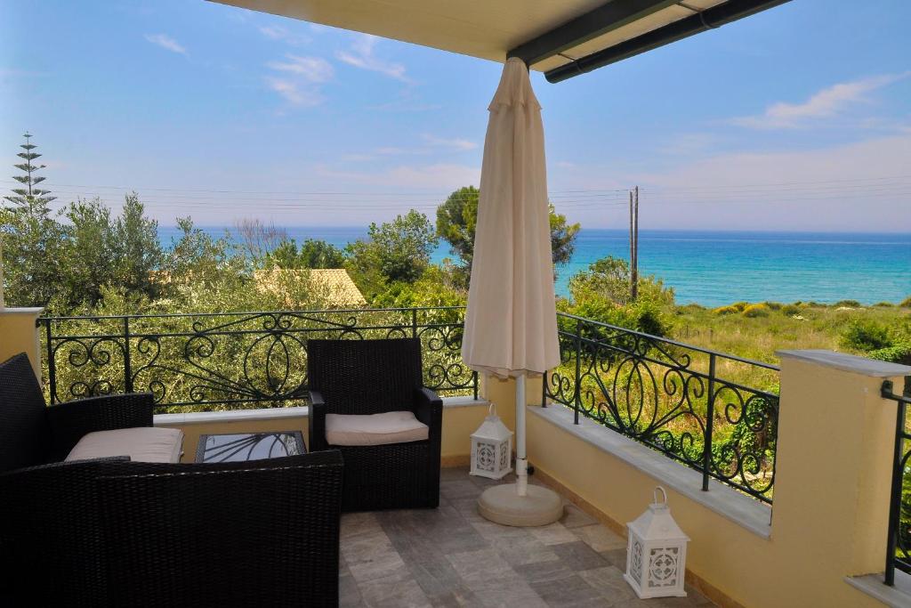a balcony with chairs and an umbrella and the ocean at Holiday House Angelos C on Agios Gordios Beach in Agios Gordios