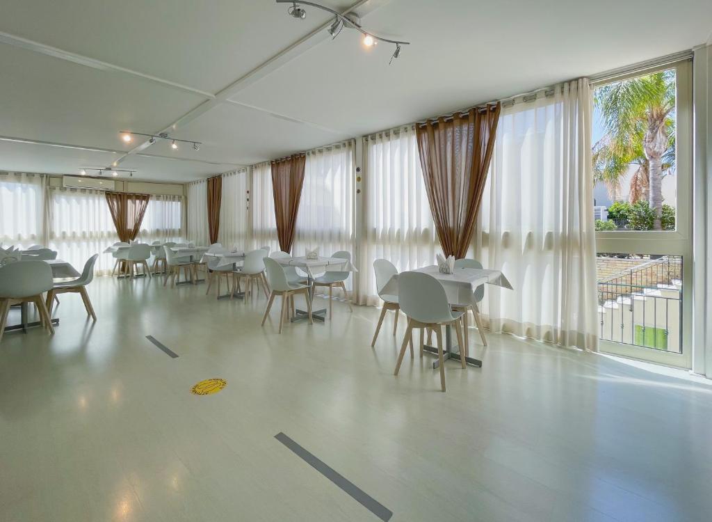 a dining room with tables and chairs and windows at Hotel Sikania in San Vito lo Capo