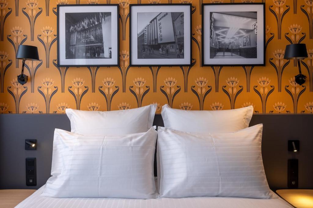 - une chambre avec deux oreillers blancs et un mur avec des photos dans l'établissement Ferdinand Hotel Tours, à Tours