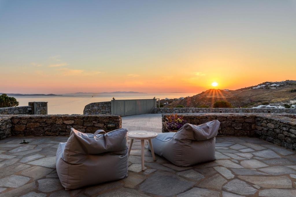 Quattro Venti Suites Mykonos في تورلوس: غروب الشمس من فناء مع كرسيين وطاولة