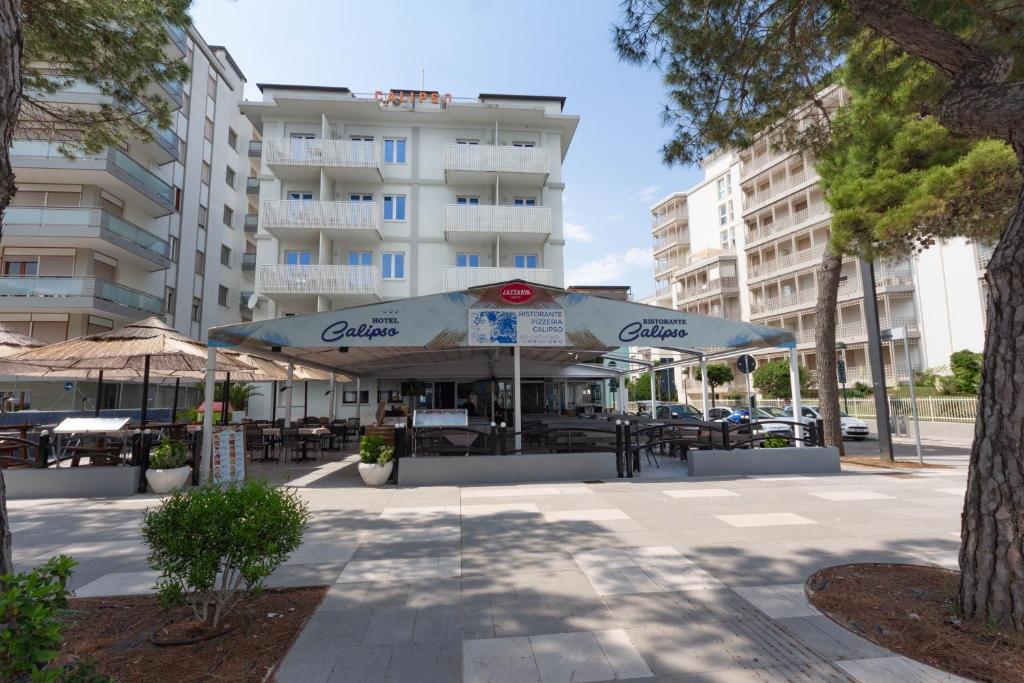 un patio con tavoli e ombrelloni di fronte a un edificio di Hotel Calipso a Lignano Sabbiadoro