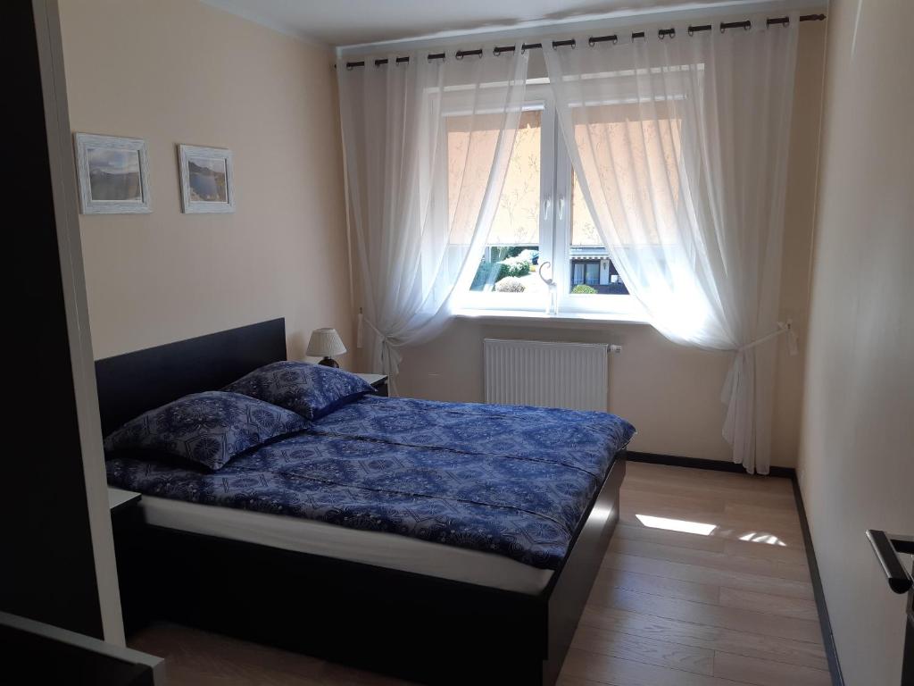 a bedroom with a bed with a blue comforter and a window at Luksusowy Apartament in Reda