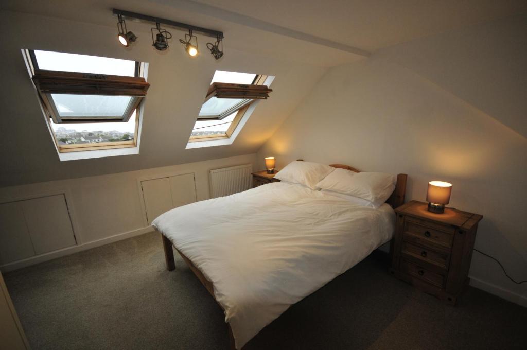 um quarto com duas janelas e uma cama com lençóis brancos em Surf View Apartment, Newquay em Newquay