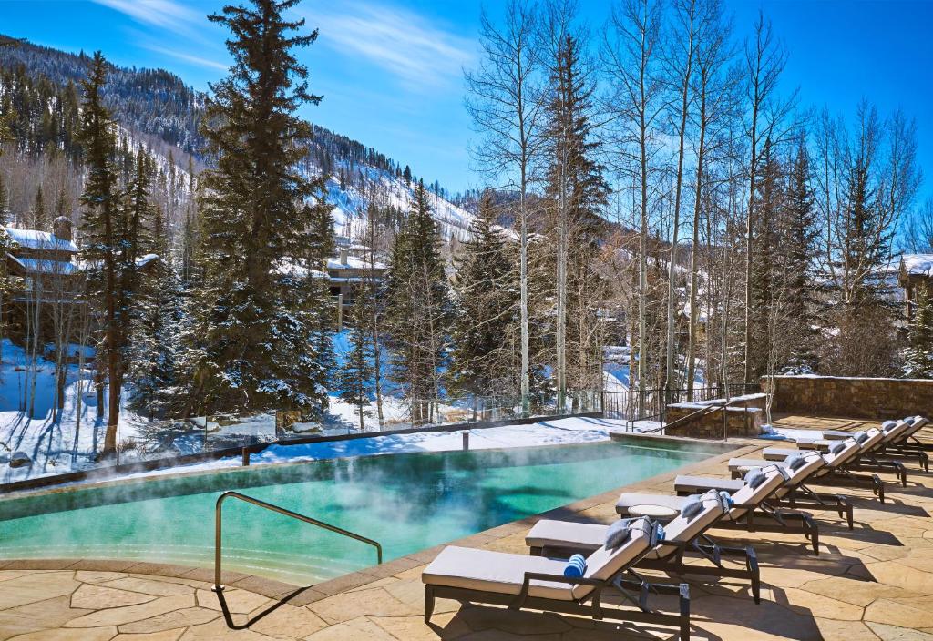 a swimming pool with lounge chairs and snow covered mountains at Vail Residences at Cascade Village, a Destination by Hyatt Residence in Vail