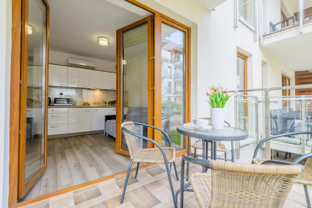 Cozy balcony café set with wicker chairs, small table holding tulips and coffee cup, open kitchen doors.