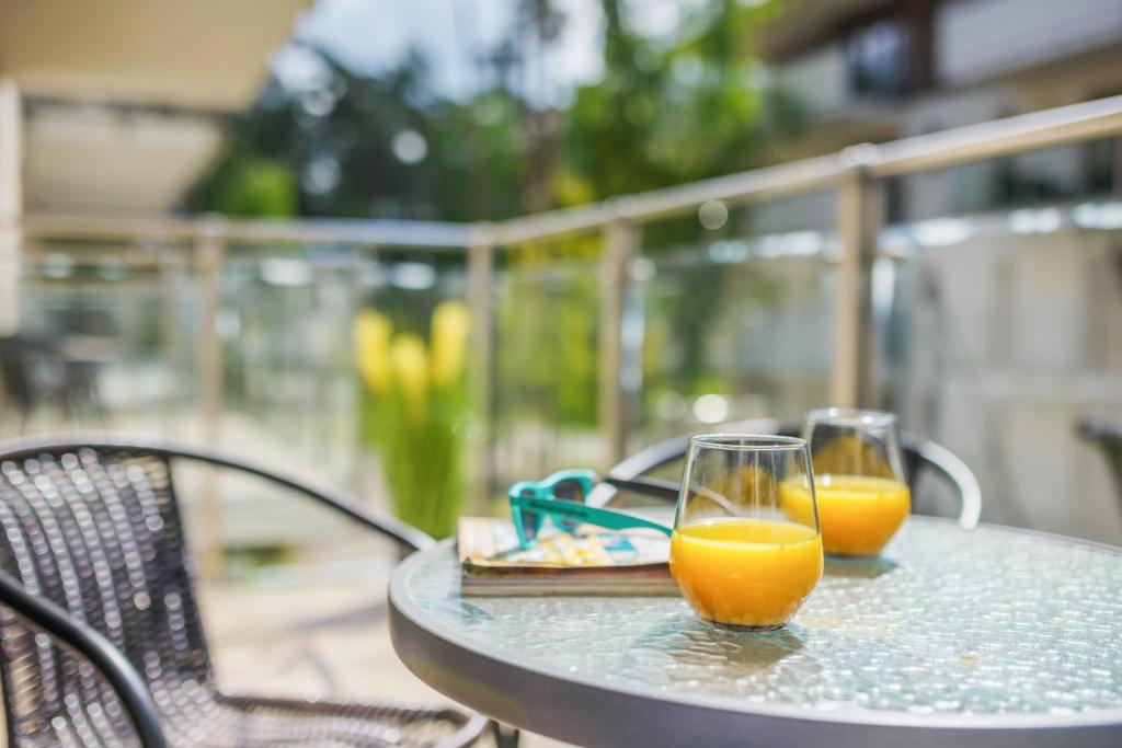 Two glasses of orange juice on glass balcony table, sunglasses and book blurred, sunny outdoor ambiance.