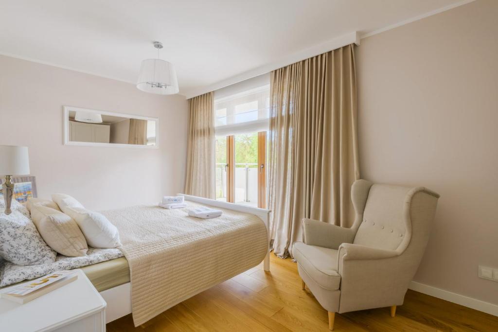 Serene beige bedroom featuring made bed, textured quilt, bedside table and comfortable wingback armchair by window.