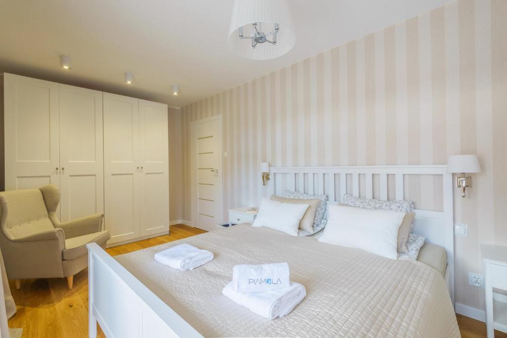 Light-filled bedroom with double bed, neatly folded towels on duvet, tall wardrobe and cozy beige armchair.