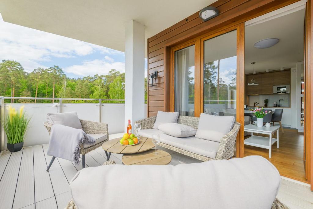 Sunny terrace with cushioned wicker sofa, round coffee tables topped with fruit and wine, interior visible.