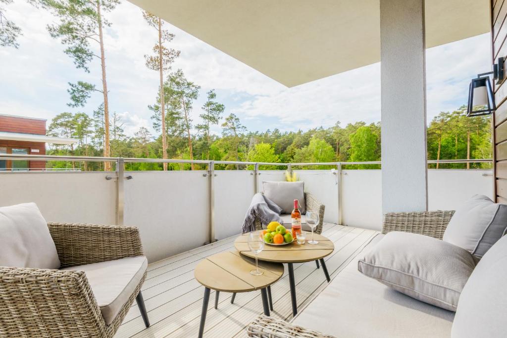 Covered balcony with wicker seating, nesting tables displaying fruit and wine, overlooking treed forest view.