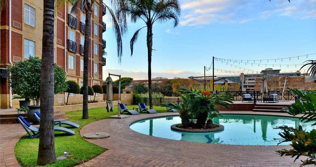 basen z krzesłami i palmami obok budynku w obiekcie ANEW Hotel Centurion Pretoria w mieście Centurion