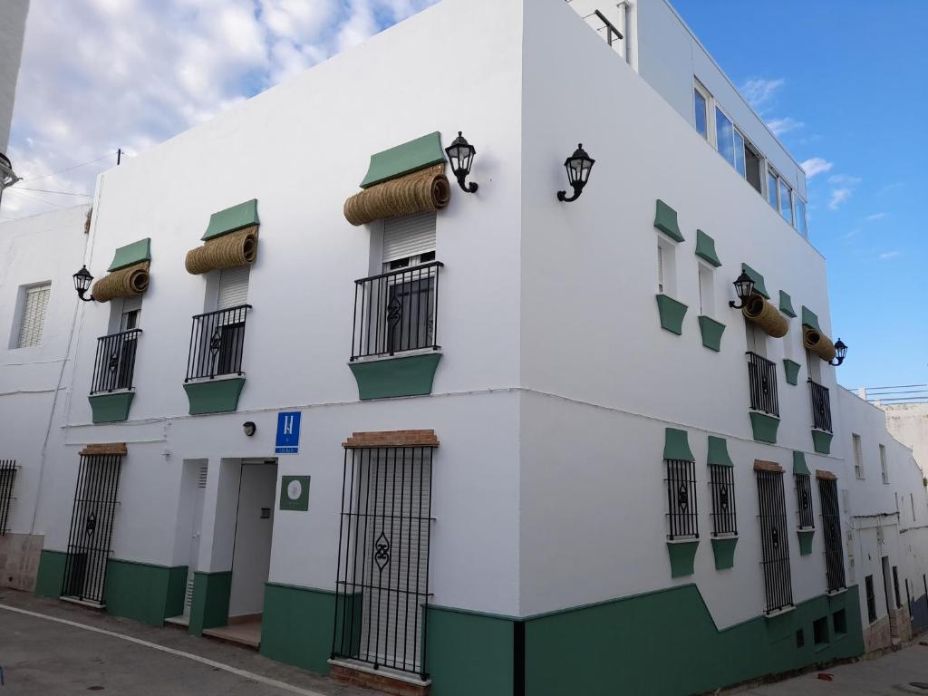 um edifício branco com janelas verdes e brancas em Hostal Casandra - antiguo Hostal Los Valencianos em Conil de la Frontera