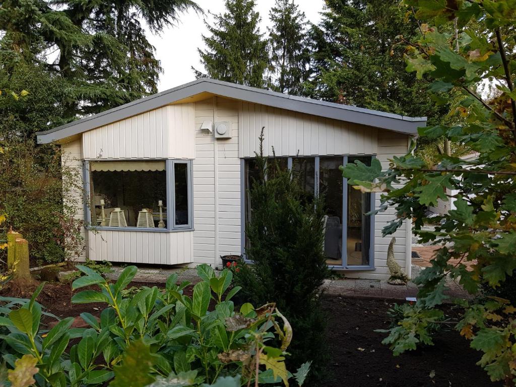 a small white shed with a window in a garden at De Blauwe Reiger mooi dubbel chalet in de Veluwse bossen in Putten