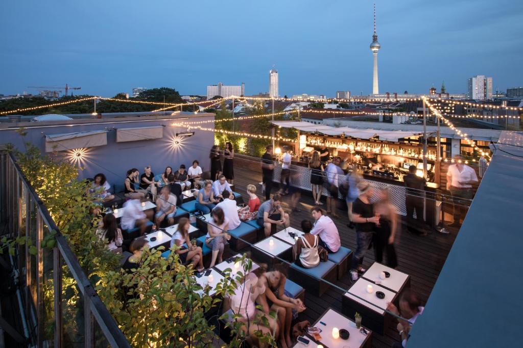 una folla di persone sedute in un bar all'ultimo piano di notte di Hotel AMANO Rooms & Apartments a Berlino