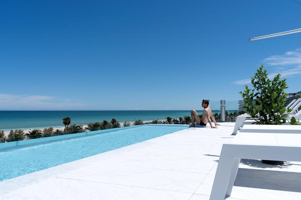 uma mulher sentada ao lado de uma piscina ao lado do oceano em PICCOLA MAESTA' boutique rooms em Civitanova Marche