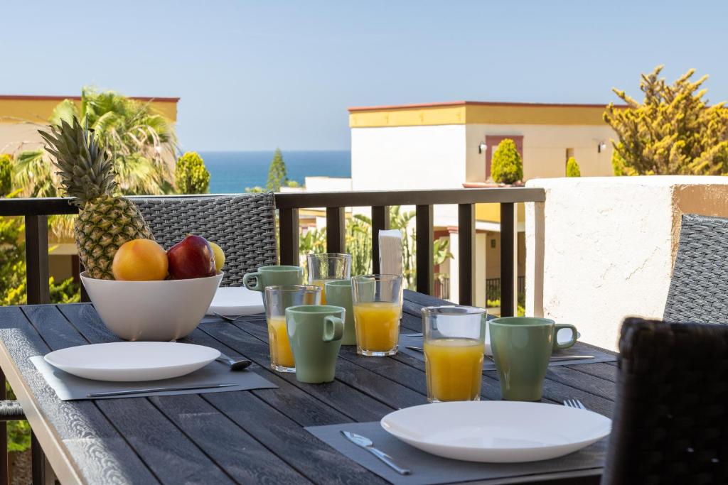einen Holztisch mit einer Schale Obst und Gläsern Orangensaft in der Unterkunft OleHolidays Romana Playa 334 vistas al mar in Marbella